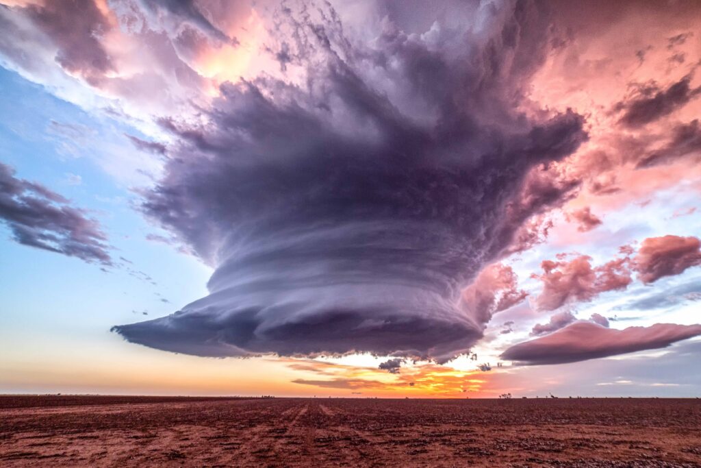 supercell storm at sunset, main cloud is lighted in purple, while the rest of the upper level clouds are pink, giving a cotton candy effect in the sky.